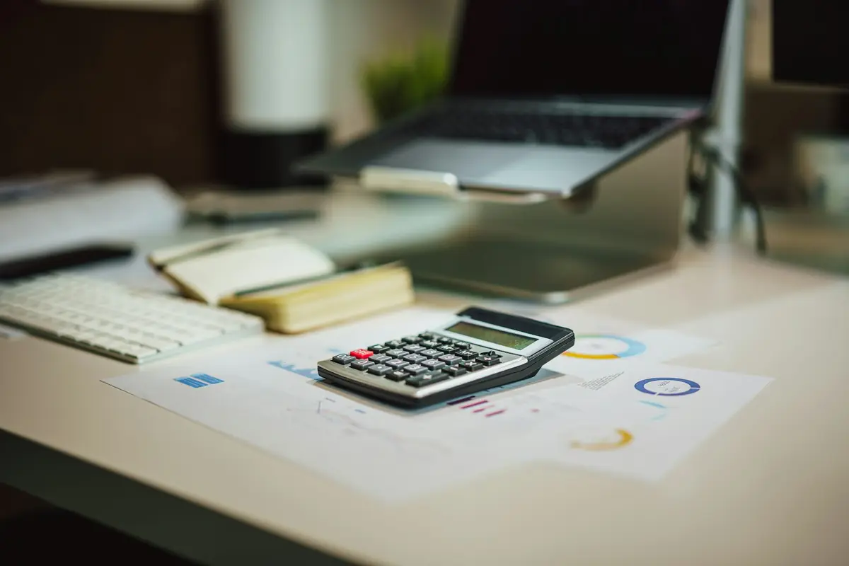 A calculator next to a laptop on a desk