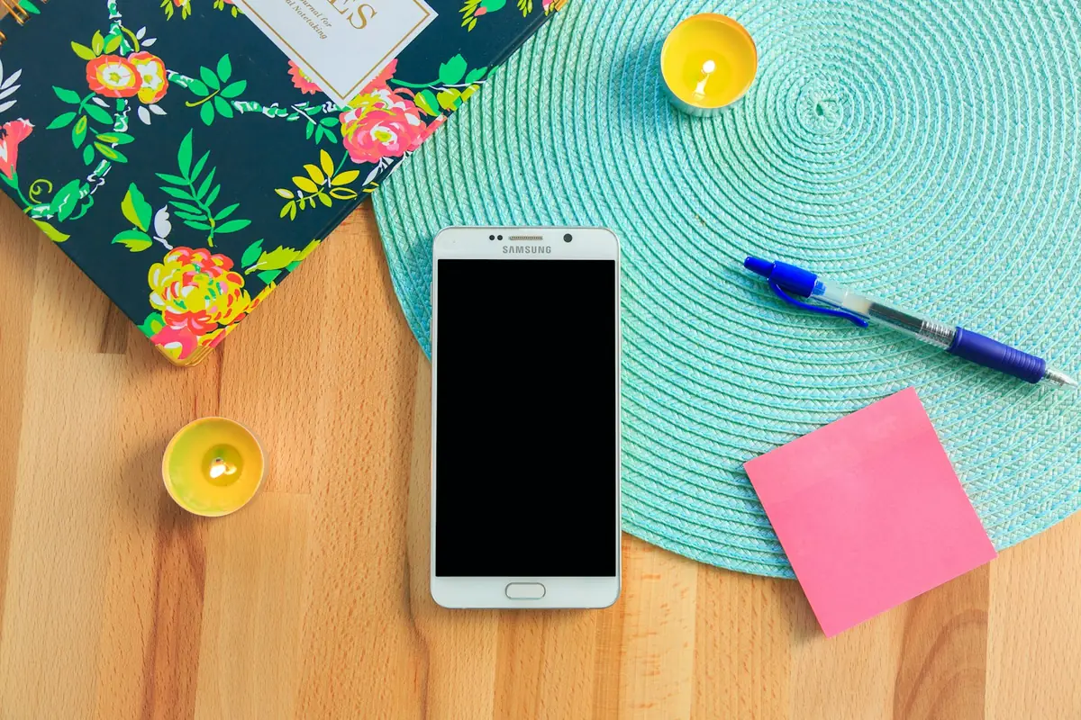 A smartphone on a table beside a pen and sticky note